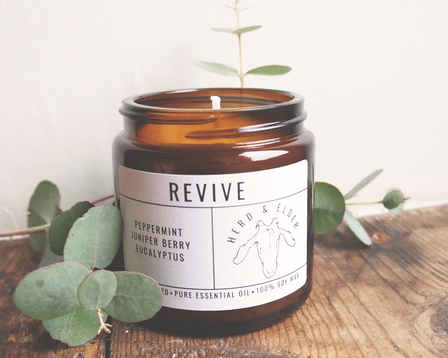 Revive - Essential Oil Eucalyptus, Peppermint & Juniper Berry Candle in amber jar with eucalyptus leaves.