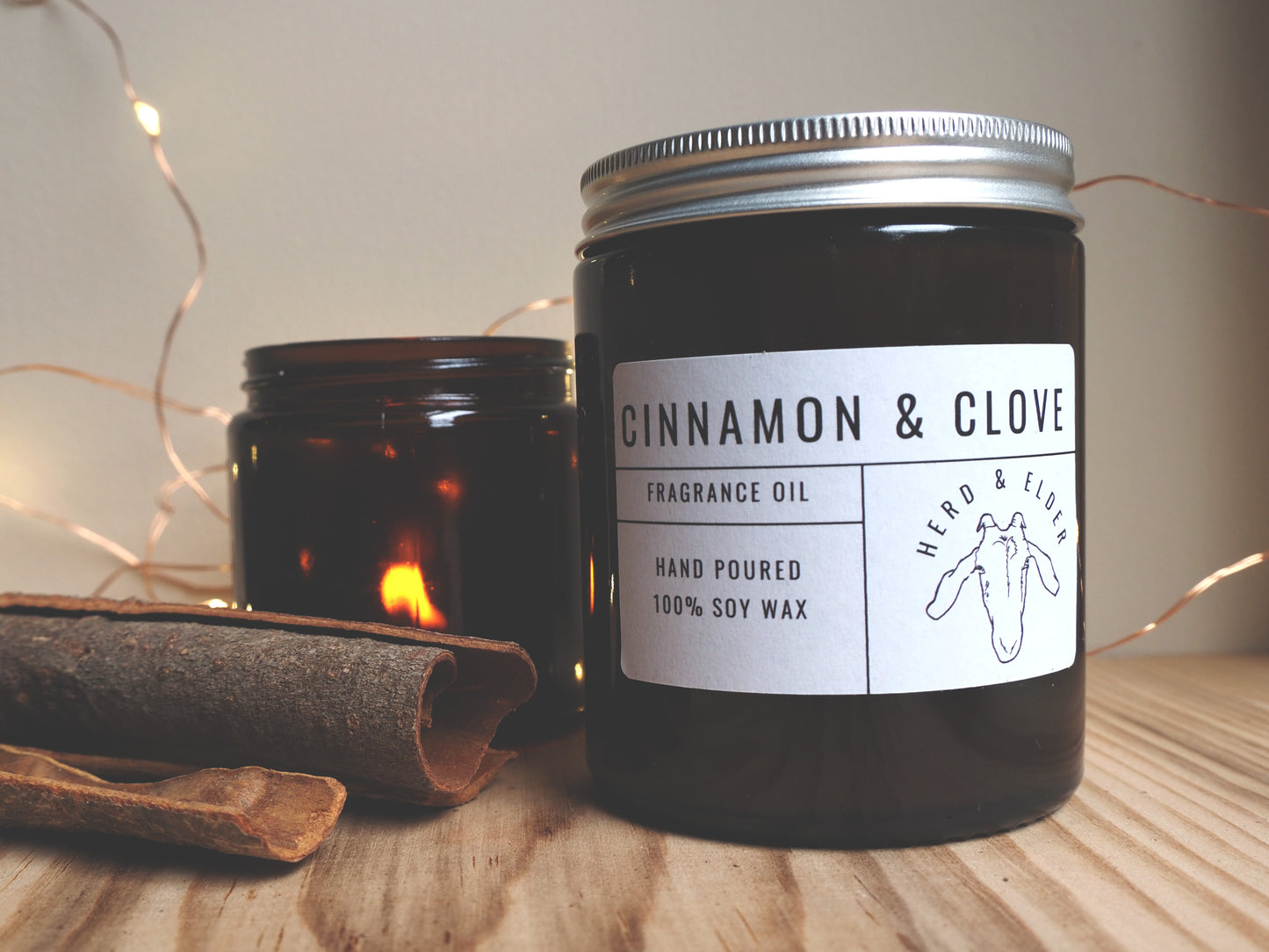 Christmas Soy Wax Candle – Cinnamon & Clove in a jar, with cinnamon sticks and soft lights in the background.