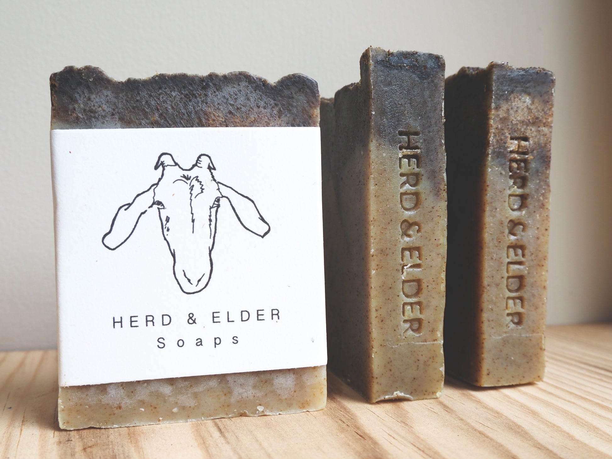 Herd & Elder goats milk soap bars displayed on wooden surface with artisanal packaging.