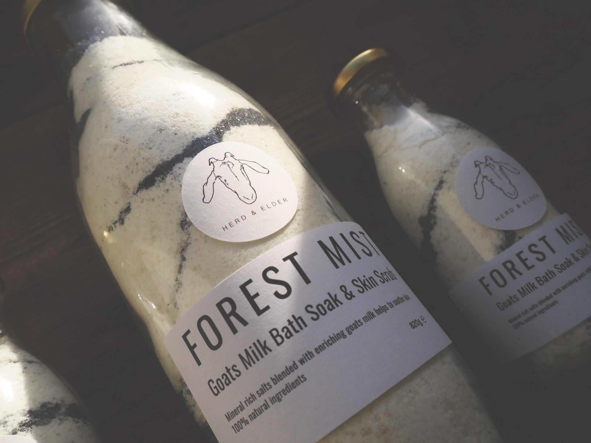 Goat Milk Bath Salts - Sandalwood & Fir Needle - Forest Mist in glass bottles on a wooden surface.